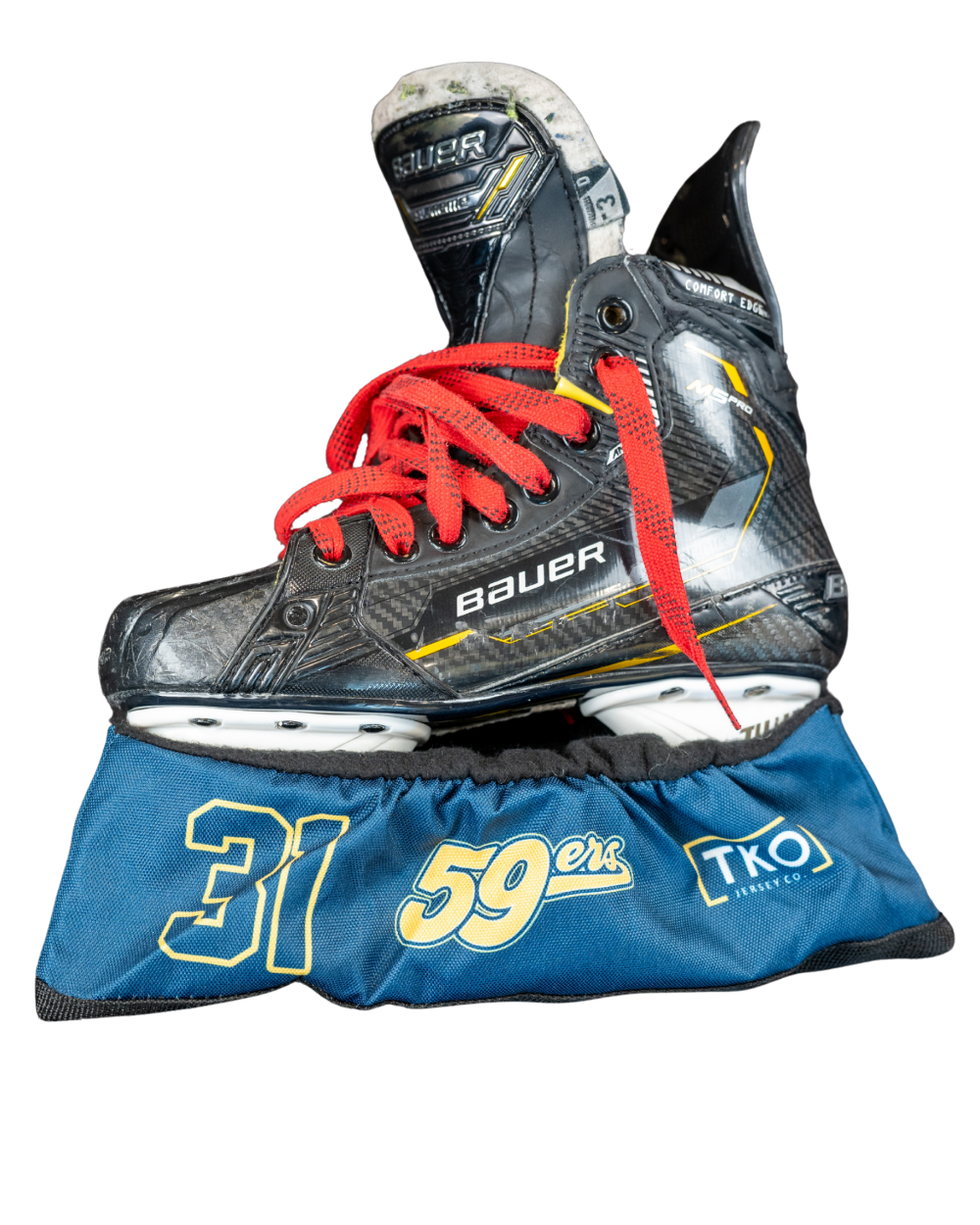 A black and gray hockey skate boot with bright red laces, resting on a blue protective skate bag with white and yellow graphics, isolated on a white background.
